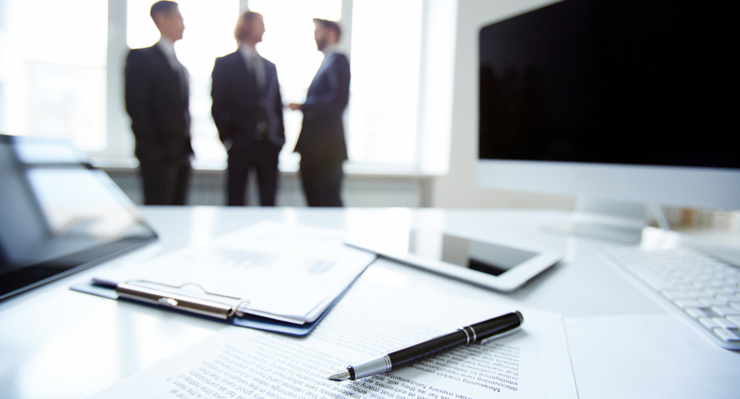 Imagen de un primer plano de un contrato con tres ejecutivos al fondo desenfocados
